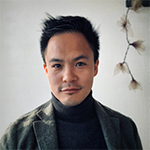 Head shot of Andrew Lee in a turtleneck and blazer, with a strand of plant hanging in the background