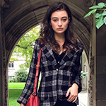 Ariel LaFayette standing in a U of T archway with a red handbag and wearing a plaid shirt