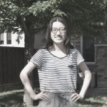 Elizabeth Zhu standing smiling in a sunny backyard, hands on her hips