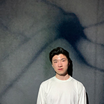 Ethan Xu standing in front of a gray wall with a cell-like shadow reflected on it as well