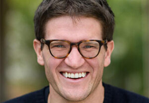 Close-up of a smiling, bespectacled Harvey Lederman in a dark blue sweater