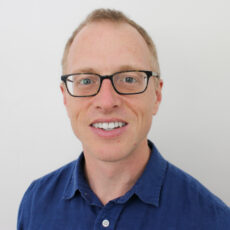 Man with close cropped hair in blue shirt and glasses