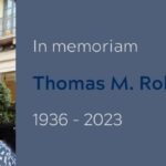Head shot of Thomas M. Robinson, a man with short white hair and beard, smiling into the camera in a blue and white patterned shirt in a Paris cafe. To the right, on a gray background, the words, In memoriam, Thomas M. Robinson, 1936-2023