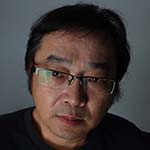 Head shot of John Han, an East Asian man with short, black hair, wearing glasses and a black top