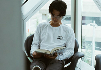 Young East Asian sitting in a chair by the window reading