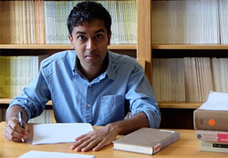 Manish Oza at a desk with bookshelves in the background