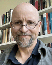 Man with glasses and beard with bookcase behind him