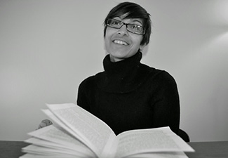 Black-and-white photo of Meena Krishnamurthy with an open book prominently displayed in front of her