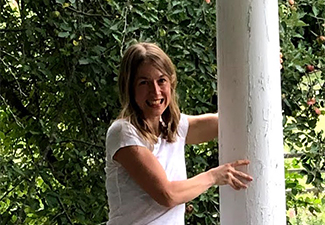 Nicole Youm in a white T-shirt standing on a porch holding onto a white column and laughing