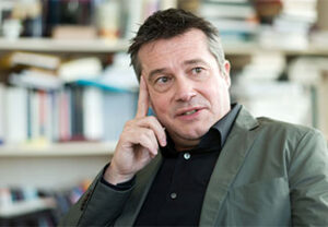 Rainer Forst in thinker pose in front of a blurred background of bookshelves