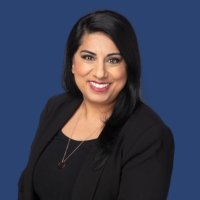 Rishma Govani, a woman with medium-length black hair in a professional black suit, stands smiling in front of a U of T blue background