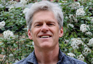 Head shot of Robert Pasnau in a blue patterned shirt in front of a bush in blossom