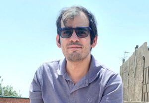 Seyed Yarandi, wearing a purple polo shirt and sunglasses, sitting on a rooftop