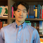Head shot of Sooyoung Moon, a younf East Asian man wearing a blue button-down shirt and standing in front of a full bookshelf.