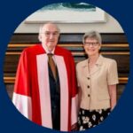 Photo of Michael Walsh in his honorary doctorate degree and his wife Virginia standing in front of a mantle, all on a U of T blue background, surrounded by the words, "Michael & Virginia Walsh Chair in History of Philosophy"