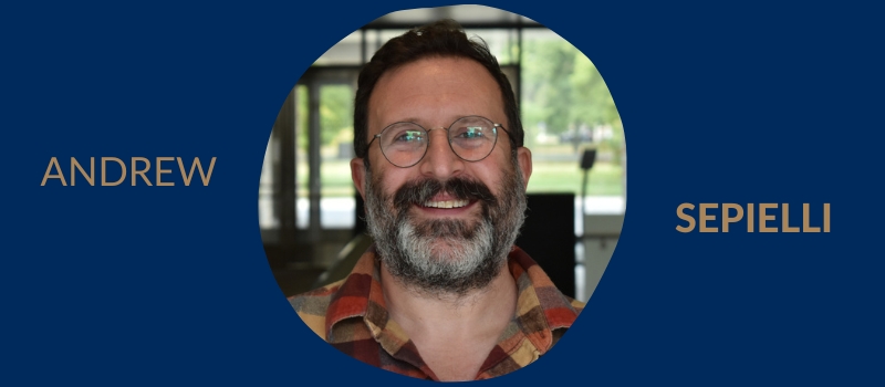 Head shot of a smiling Andrew Sepielli, gray beard and spectacles wearing a plaid shirt, on a U of T blue background and his name.
