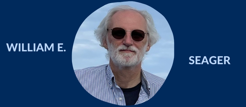 Head shot of Bill Seager, an sporting white hair and beard, sunglasses, and a blue-and-white striped button-down shirt over a black T-shirt, on a U of T blue background