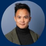 Headshot of Andrew Y. Lee, a young East Asian man wearing a blazer over top a black turtleneck and standing against a blue wall.