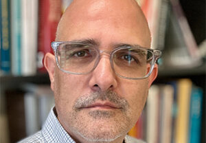 Close crop of Hagop Sarkissian, a middle-aged bald man with a slight, gray goatee and glasses, looking into the camera in front of a bookshelf.