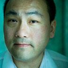 Man with short hair and shirt with blue-green light in background