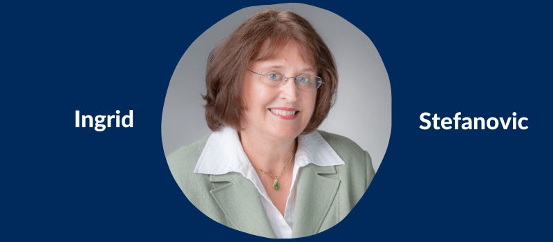 On a U of T blue background, a professional head shot of Ingrid Stefanovic, a middle-aged white woman with medium-length reddish-brown hair and glasses, smiling and wearing business attire.