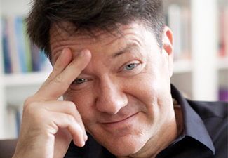 Close crop of Trenton Merricks, a middle-aged white man with short brown hair, wearing a dark button-down shirt and looking full of whimsy into the camera, in a modified thinker's pose.